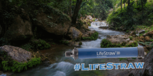 A LifeStraw Personal Water Purifier is shown in the foreground of a forest stream, highlighting its reliability for outdoor adventures. The hashtag #LifeStraw appears at the bottom, making it a must-have gear for 2025 explorers.