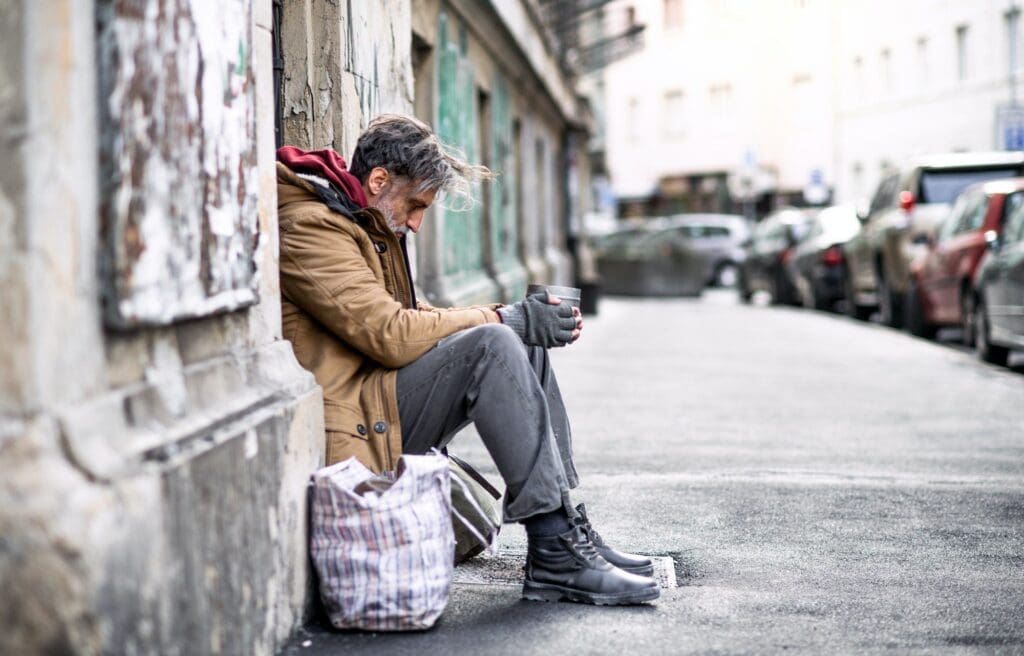 Homeless beggar man sitting outdoors in city asking for money donation.