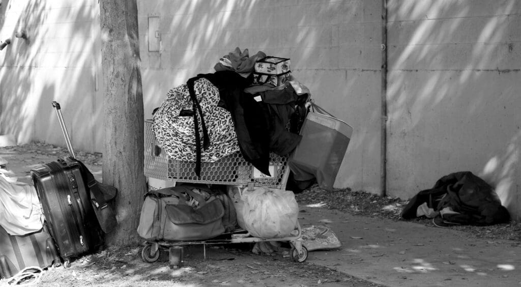 Monochromatic image of resting place of homeless person who's belongings are in a shopping cart.