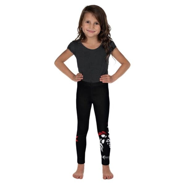 A little girl wearing black leggings in MW Combatives Kid's Spats stands against a white background.