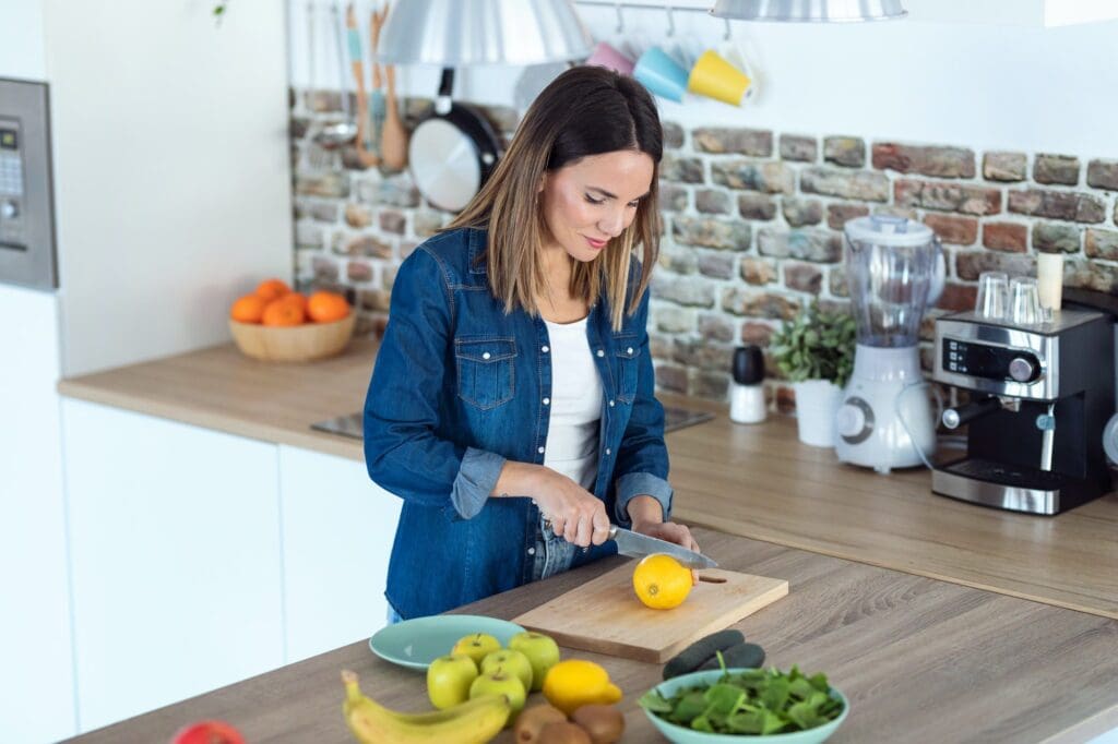 Pretty young woman cutting lemons for preparing detox beverage in the kitchen at home.