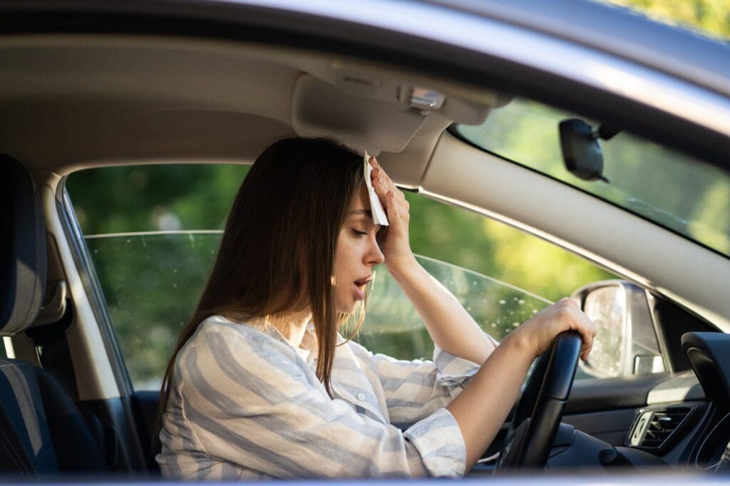 Woman driver being hot during heat wave in car, suffering from hot weather wipes sweat from forehead