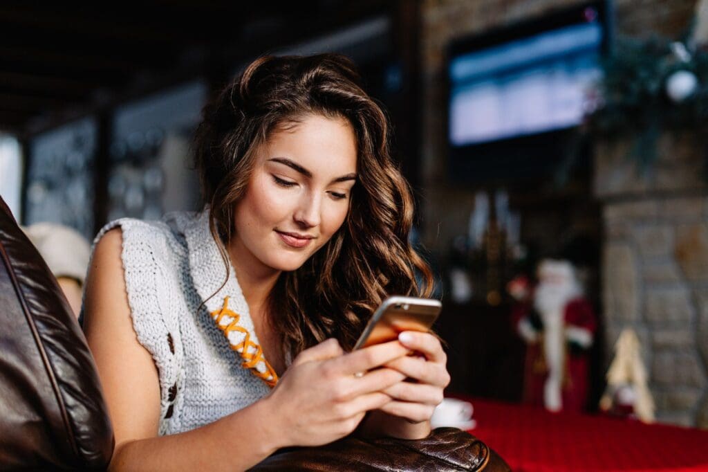 Happy young woman looking at mobile phone in bed