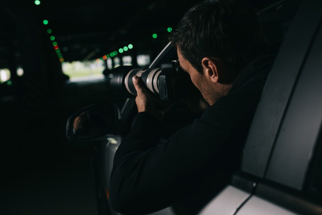 rear view of male paparazzi spying by camera with object glass from his car