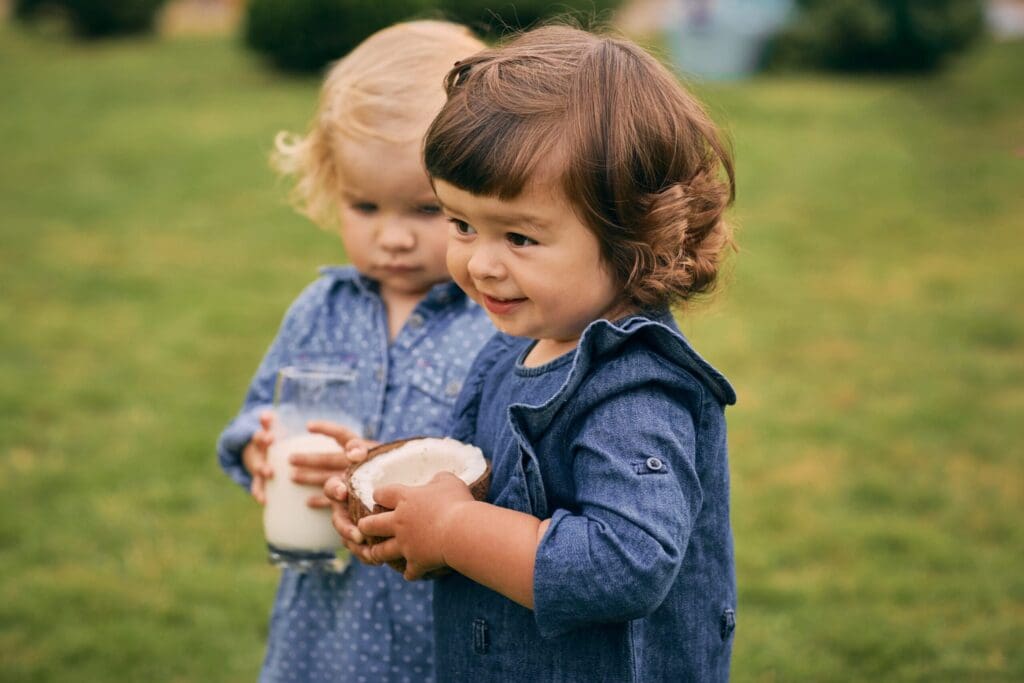 Two little girls holding a glass of coconut milk and coconut in their hands