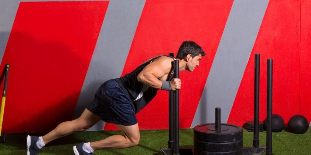 Man pushing a weighted sled at a gym.