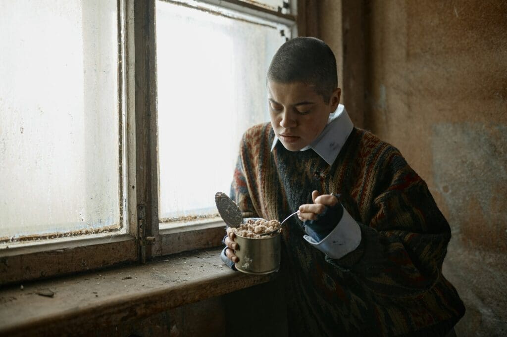 Poor unhappy young woman eating canned food against window