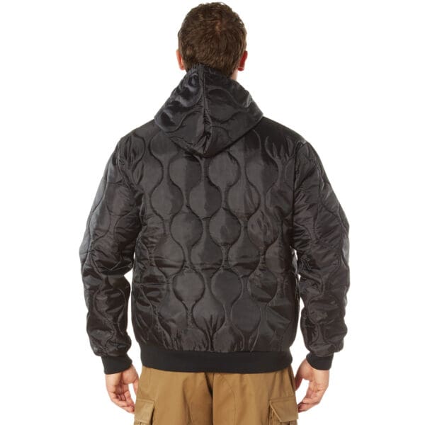 A person wearing a black Rothco quilted hooded jacket and brown pants is shown from the back.