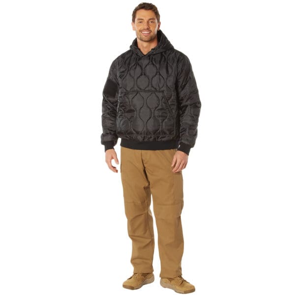 A person wearing a black Rothco quilted hoodie, brown pants, and tan shoes stands smiling against a white background.