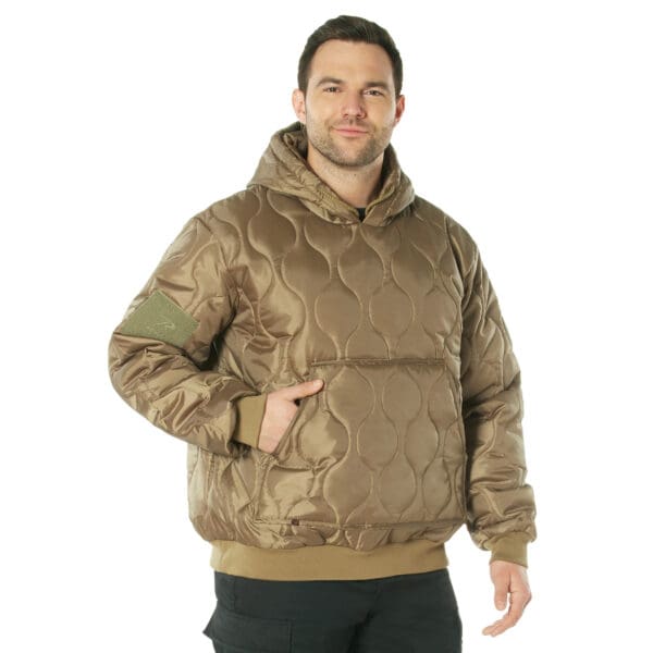 A person wearing a brown quilted woobie hoodie with hands in the front pocket stands against a white background.