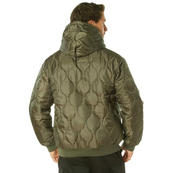 The image shows a person wearing a green, quilted hoodie with a hood, viewed from the back. The style resembles that of a cozy Woobie Sweatshirt, combining warmth and comfort seamlessly.