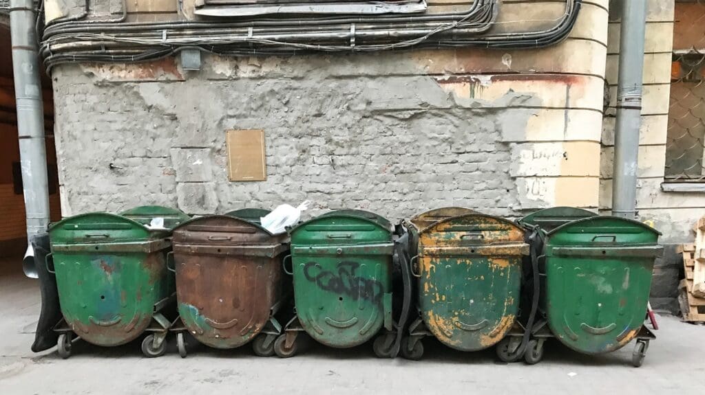 Five green dirty trash dumpsters. Old bins