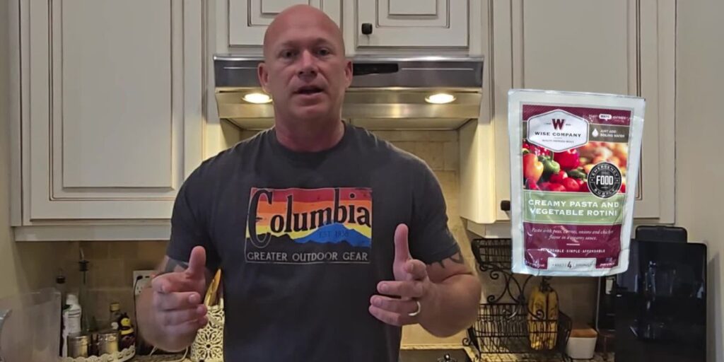 A person in a kitchen wearing a Columbia T-shirt gestures with hands, showcasing their prepper skills. On the right, a package of creamy pasta and vegetable rotini is highlighted.